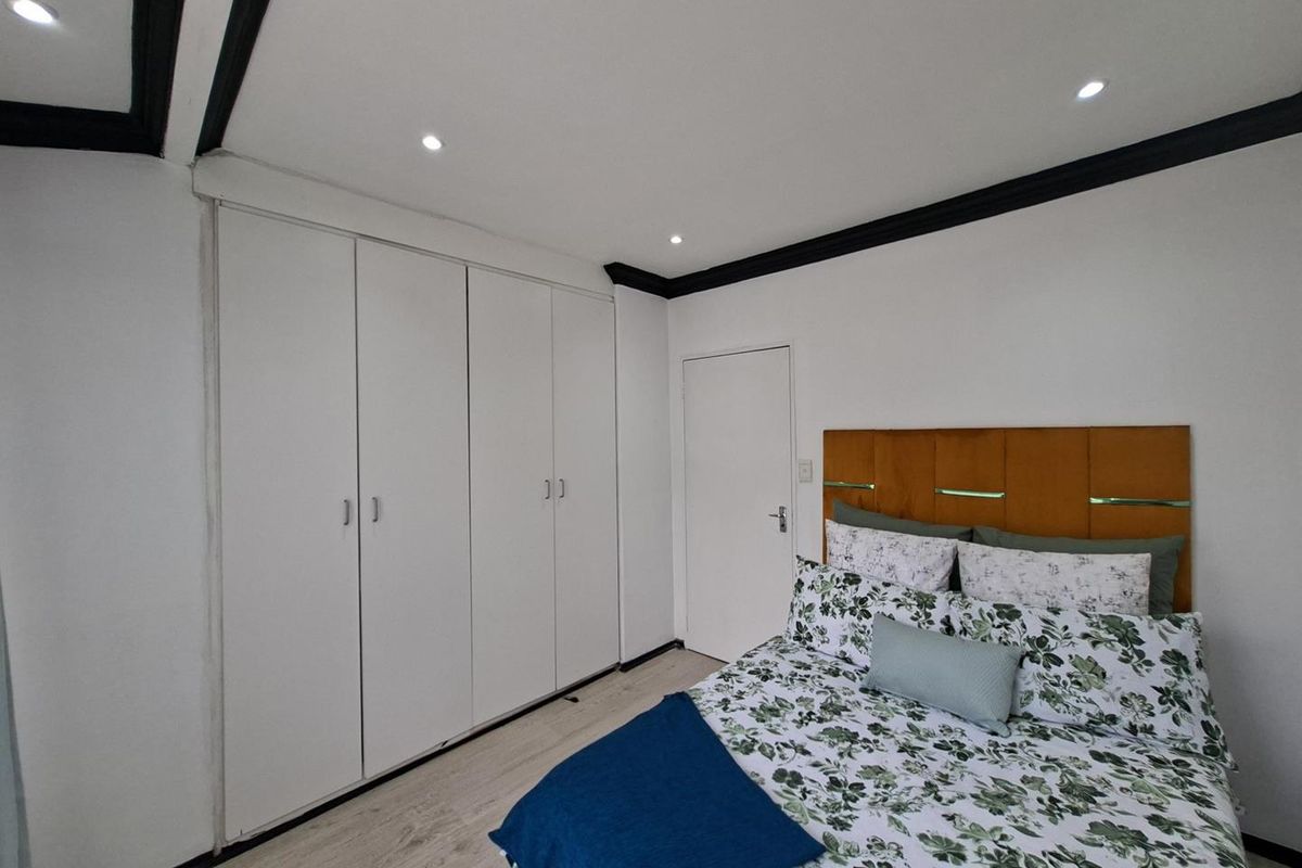 A well-maintained bedroom featuring built-in floor-to-ceiling wardrobes, recessed downlighting, and modern crown molding.