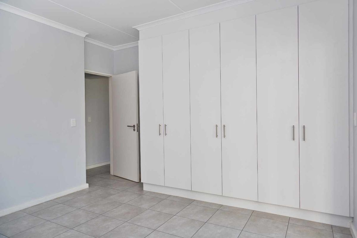 A clean, neutral bedroom featuring large floor-to-ceiling built-in cupboards and tiled flooring, offering ample storage space.