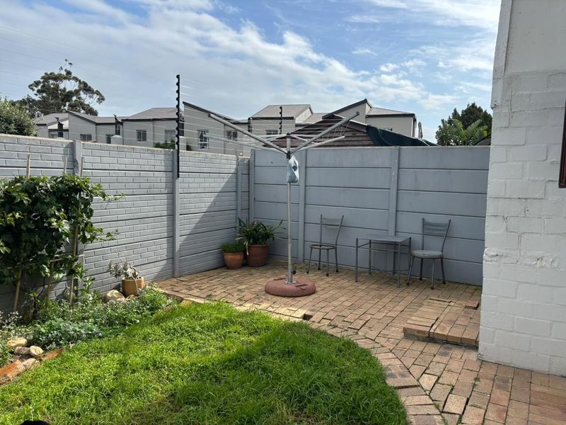 A private rear courtyard featuring brick paving, a small lawn area, and secure precast concrete boundary walls with electric fencing.
