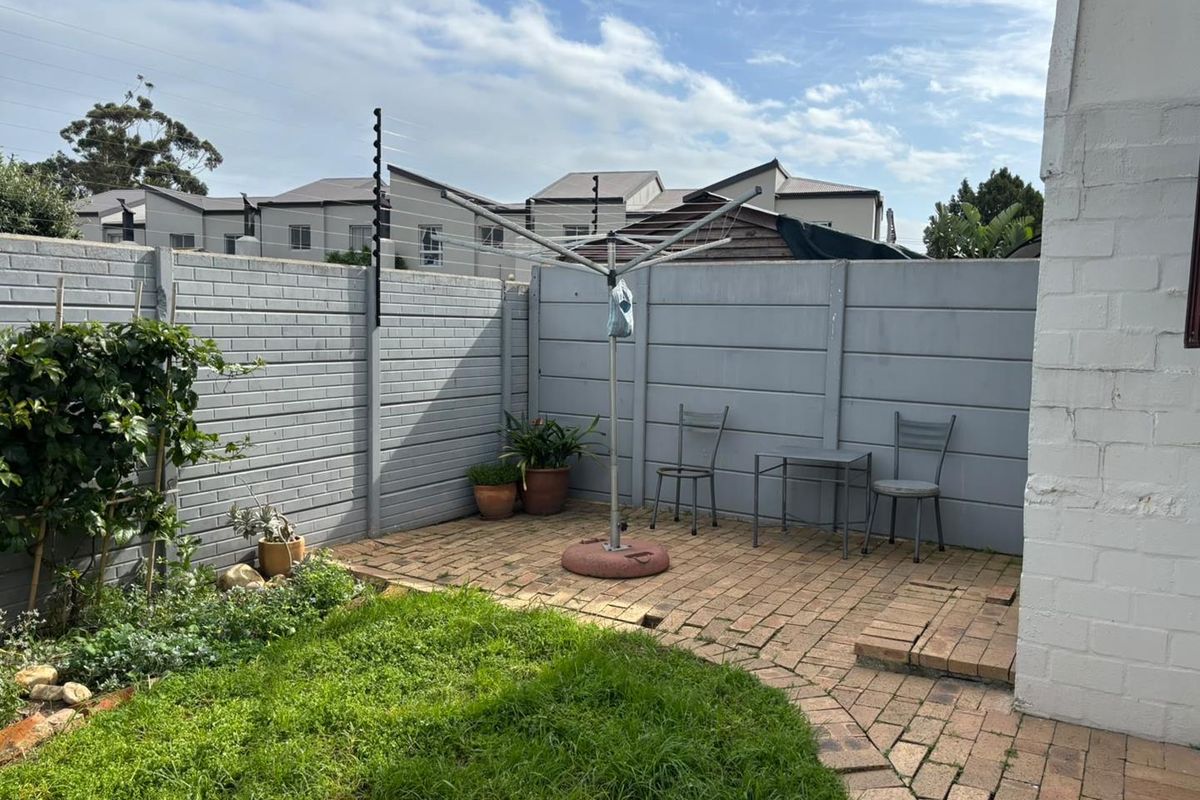 A private rear courtyard featuring brick paving, a small lawn area, and secure precast concrete boundary walls with electric fencing.