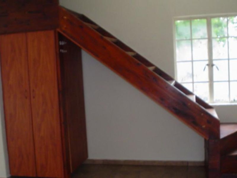 A bedroom featuring a built-in wooden cupboard and a wooden staircase leading to a loft area, with a window providing natural light.