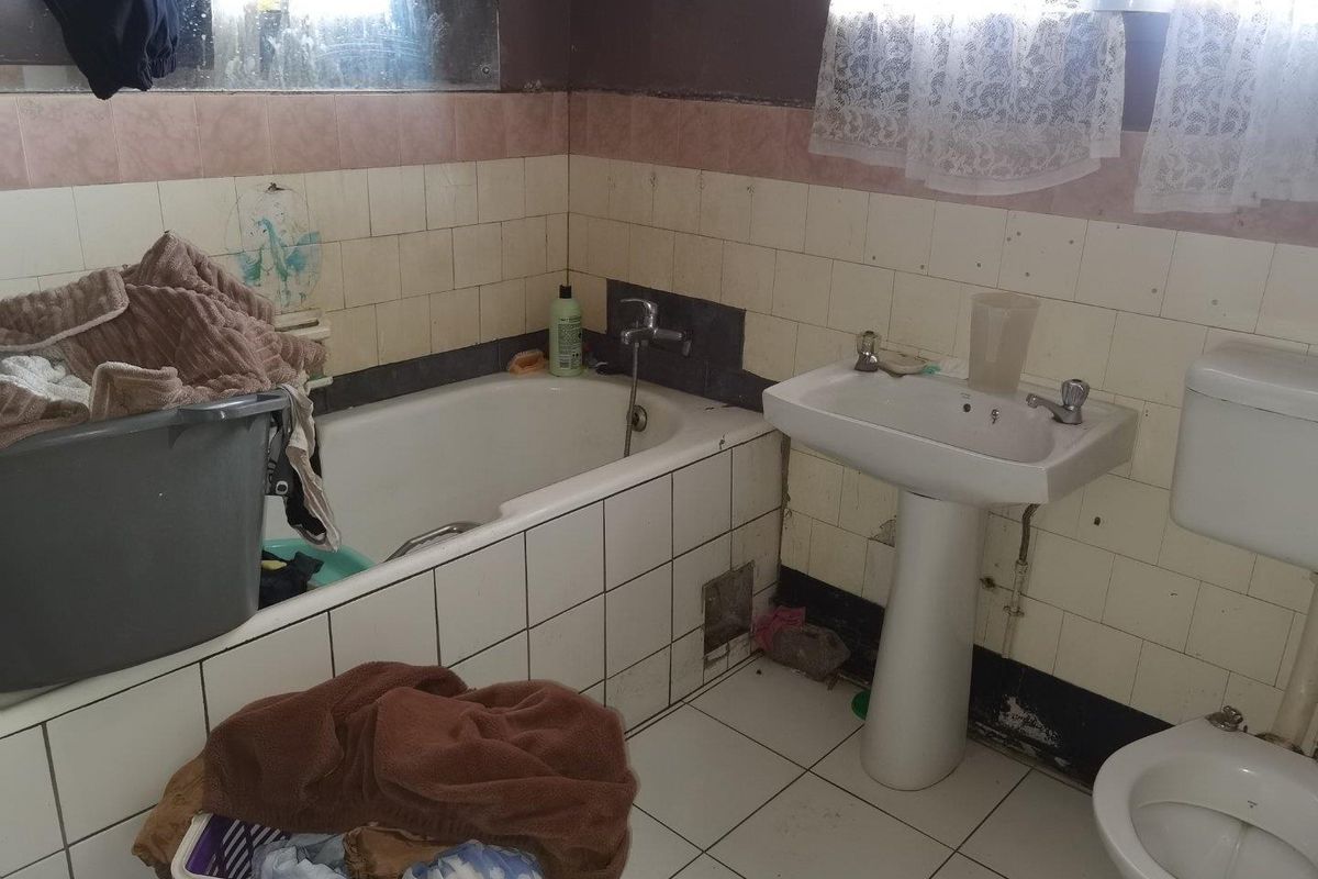 A dated bathroom featuring a standard bathtub, pedestal basin, and toilet, requiring significant renovation and cosmetic updates to restore functionality and appeal.