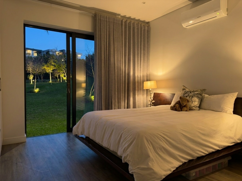 A well-maintained bedroom featuring laminate flooring, a wall-mounted air conditioning unit, and a large sliding glass door providing direct access to the garden.