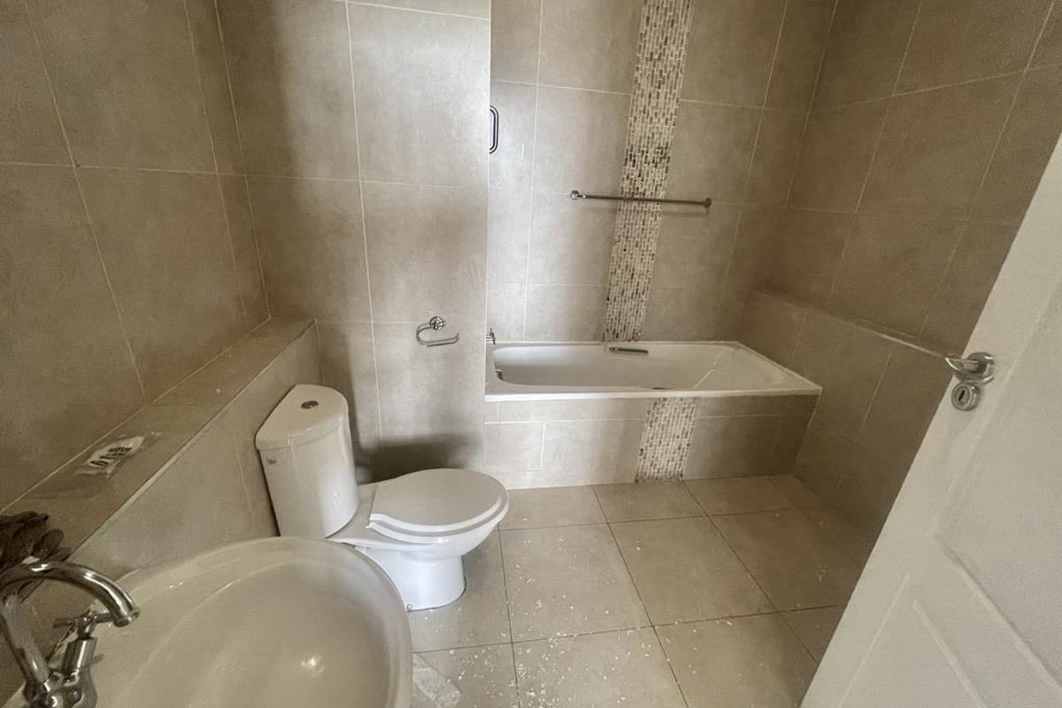A neutral-toned bathroom featuring a built-in bathtub, pedestal washbasin, and dual-flush toilet, finished with floor-to-ceiling ceramic wall tiles.