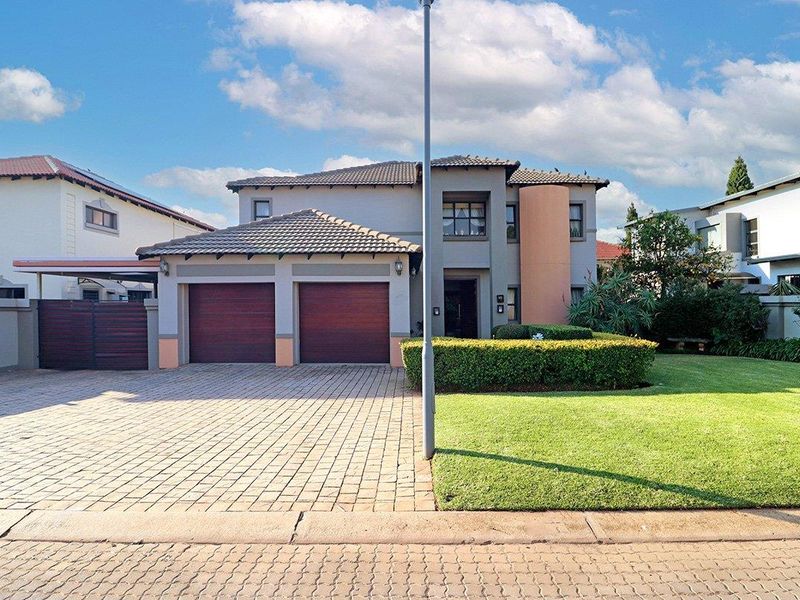 Front elevation of a two-story residential property featuring a double garage, paved driveway, and a well-maintained front garden.