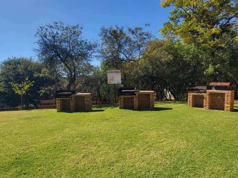 Communal garden area featuring multiple built-in brick braai stands set within a landscaped lawn with mature trees.