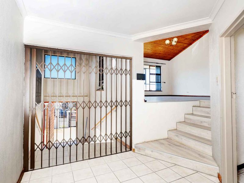 Entrance foyer featuring tiled flooring, a security gate, and a staircase leading to an elevated living area with a timber-paneled ceiling.