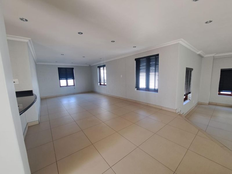 Spacious open-plan living area featuring neutral tiled flooring, recessed downlighting, and fitted venetian blinds, offering a versatile layout for modern living.