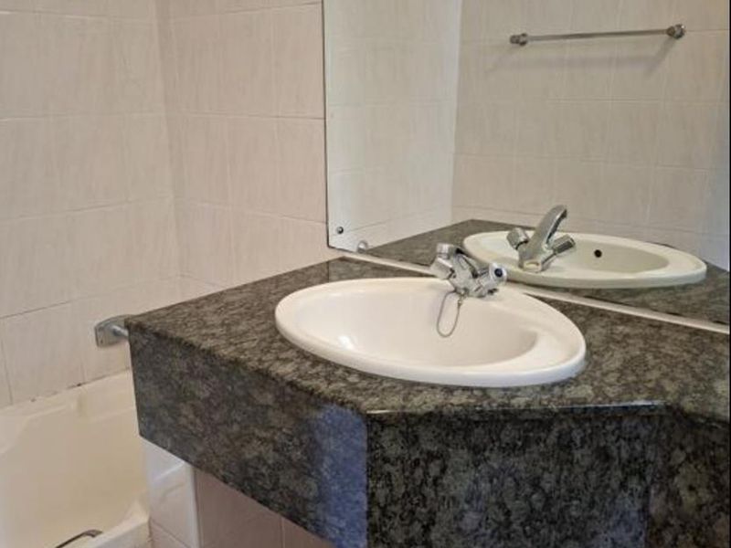 A functional bathroom featuring a granite vanity countertop, drop-in sink, tiled walls, and a built-in bathtub.