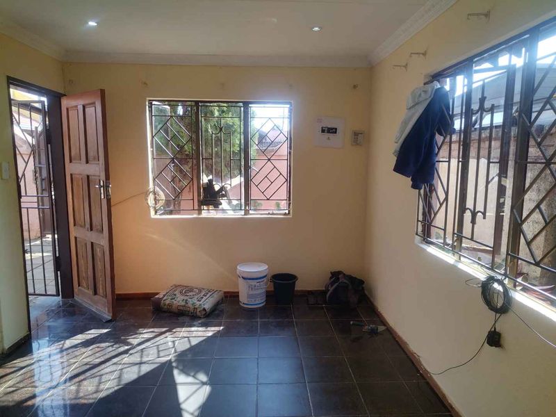 An empty living room featuring dark tiled flooring, security bars on windows, and recessed lighting, presenting a blank canvas for renovation.