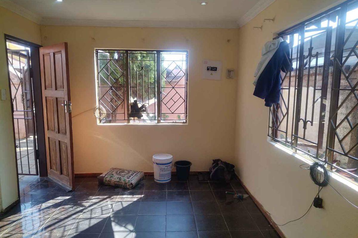 An empty living room featuring dark tiled flooring, security bars on windows, and recessed lighting, presenting a blank canvas for renovation.