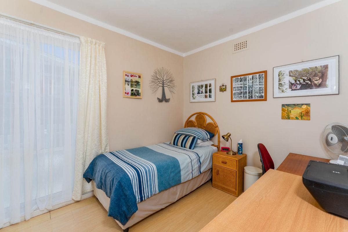 A functional bedroom featuring light-toned laminate flooring, neutral wall paint, and a sliding glass door providing access to the exterior.