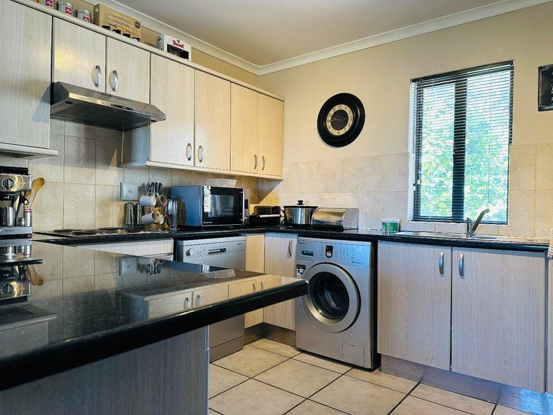 A functional kitchen featuring light wood-finish cabinetry, dark granite countertops, tiled backsplash, and integrated space for laundry and dishwashing appliances.
