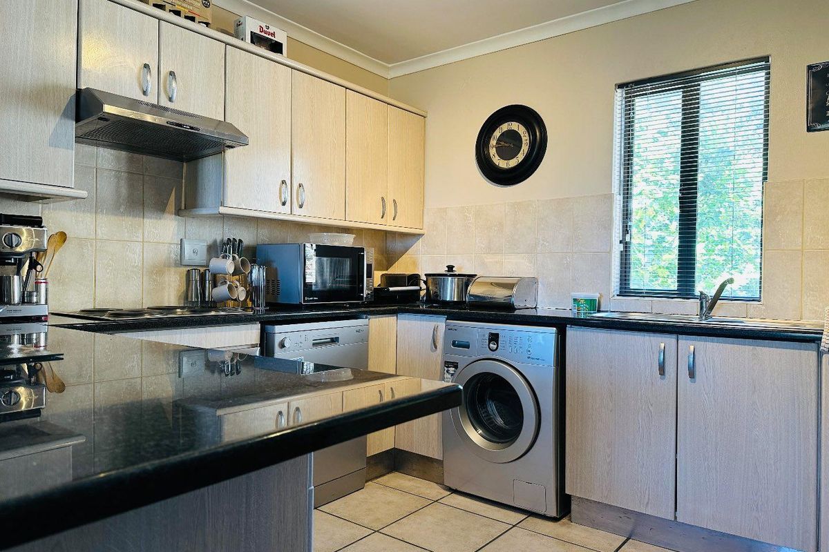 A functional kitchen featuring light wood-finish cabinetry, dark granite countertops, tiled backsplash, and integrated space for laundry and dishwashing appliances.