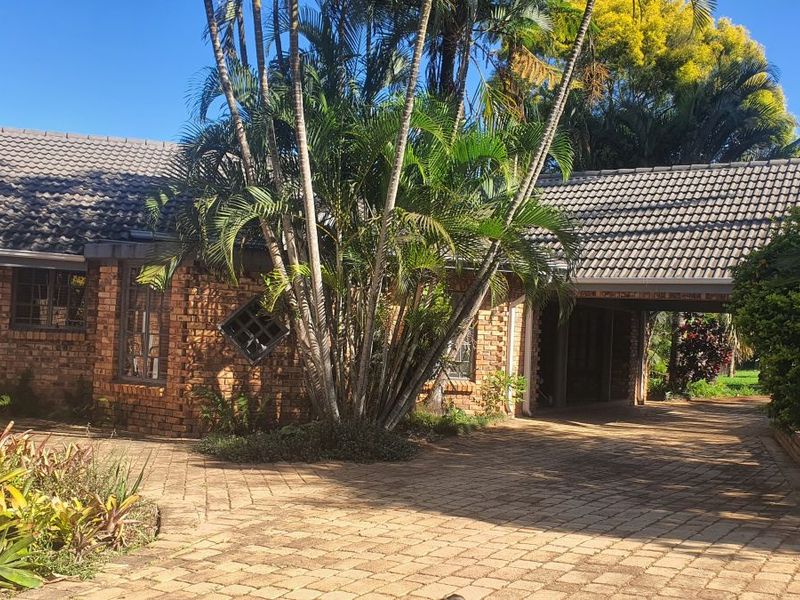 A charming face brick house featuring a tiled roof, a paved driveway, and a convenient carport, surrounded by established garden landscaping.