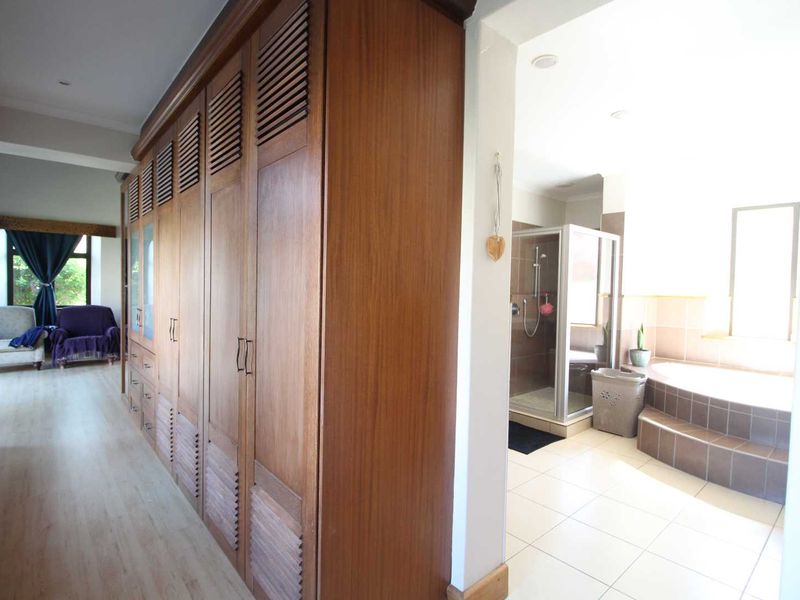 Spacious bedroom featuring extensive built-in wooden cabinetry and an en-suite bathroom with a shower and built-in bathtub.