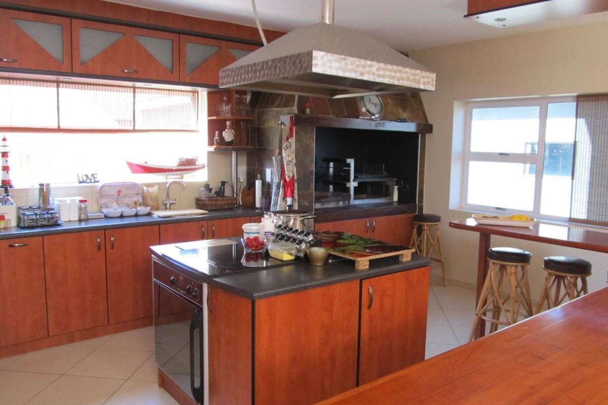 Spacious kitchen featuring wooden cabinetry, a central island with built-in oven and cooktop, and a large integrated indoor braai area with extractor hood.