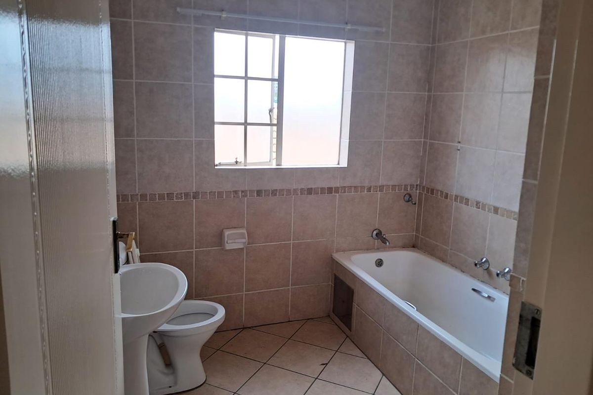 A functional bathroom featuring a built-in bathtub, pedestal basin, and toilet with neutral wall and floor tiling.