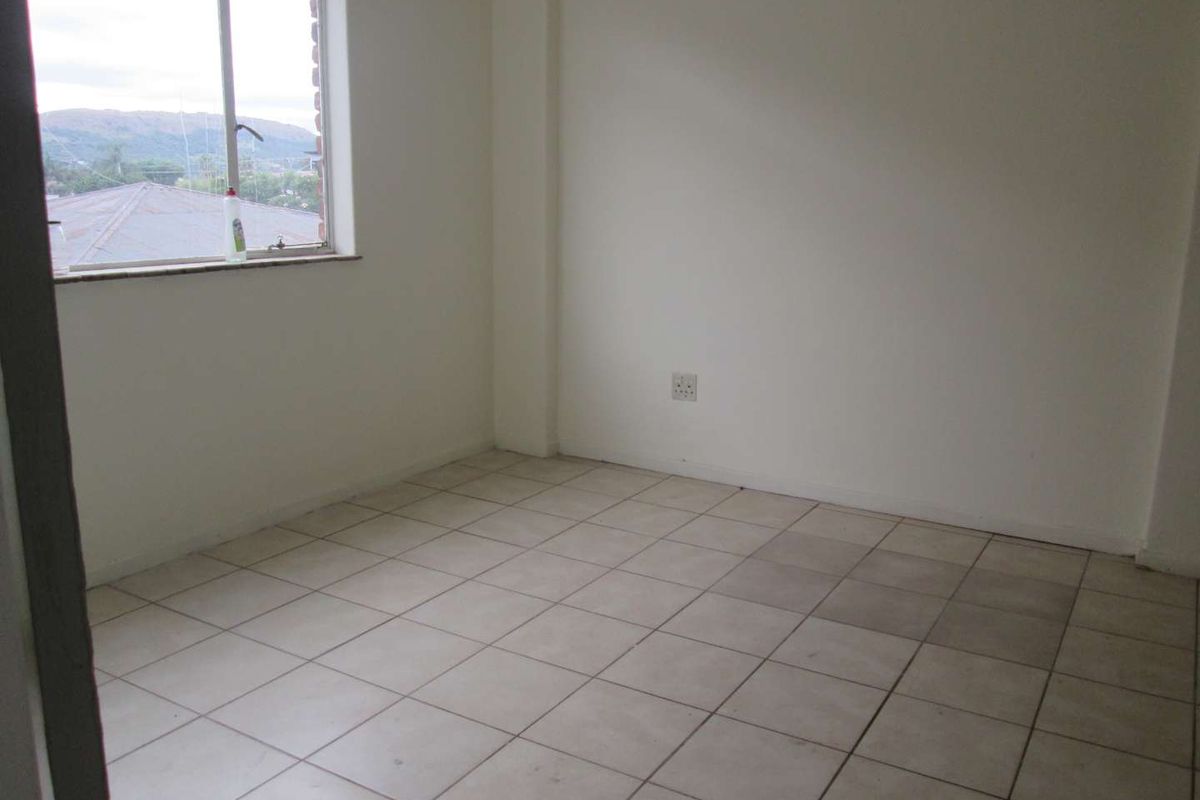 An empty bedroom featuring neutral tiled flooring, plain white walls, and a window providing natural light and neighborhood views.