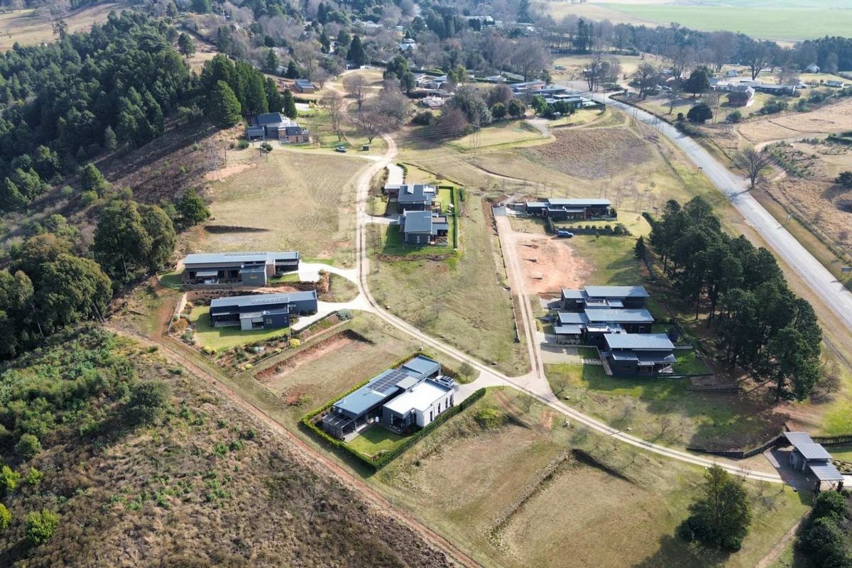 An aerial view of a residential estate featuring multiple modern homes situated on large, landscaped plots with surrounding natural vegetation and access roads.