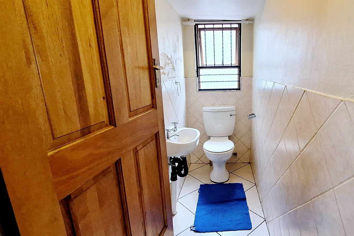 A compact guest bathroom featuring a pedestal sink, toilet, and tiled walls with a security-barred window.