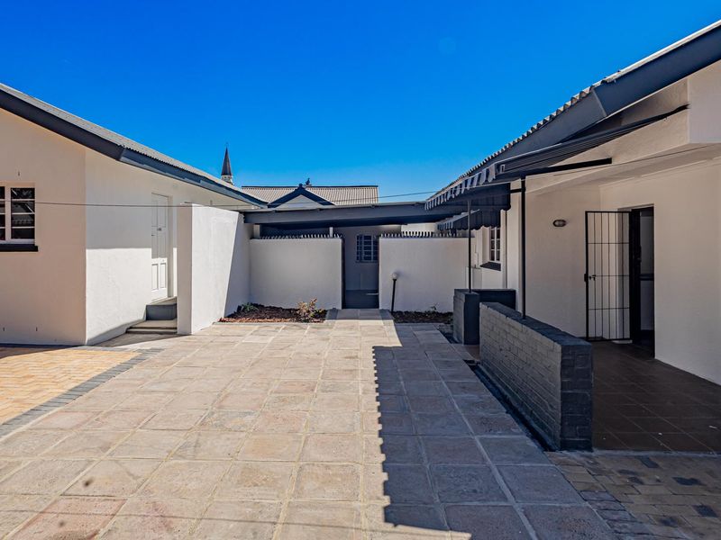 A well-maintained paved rear courtyard featuring a covered patio area, secure access points, and clean exterior finishes.