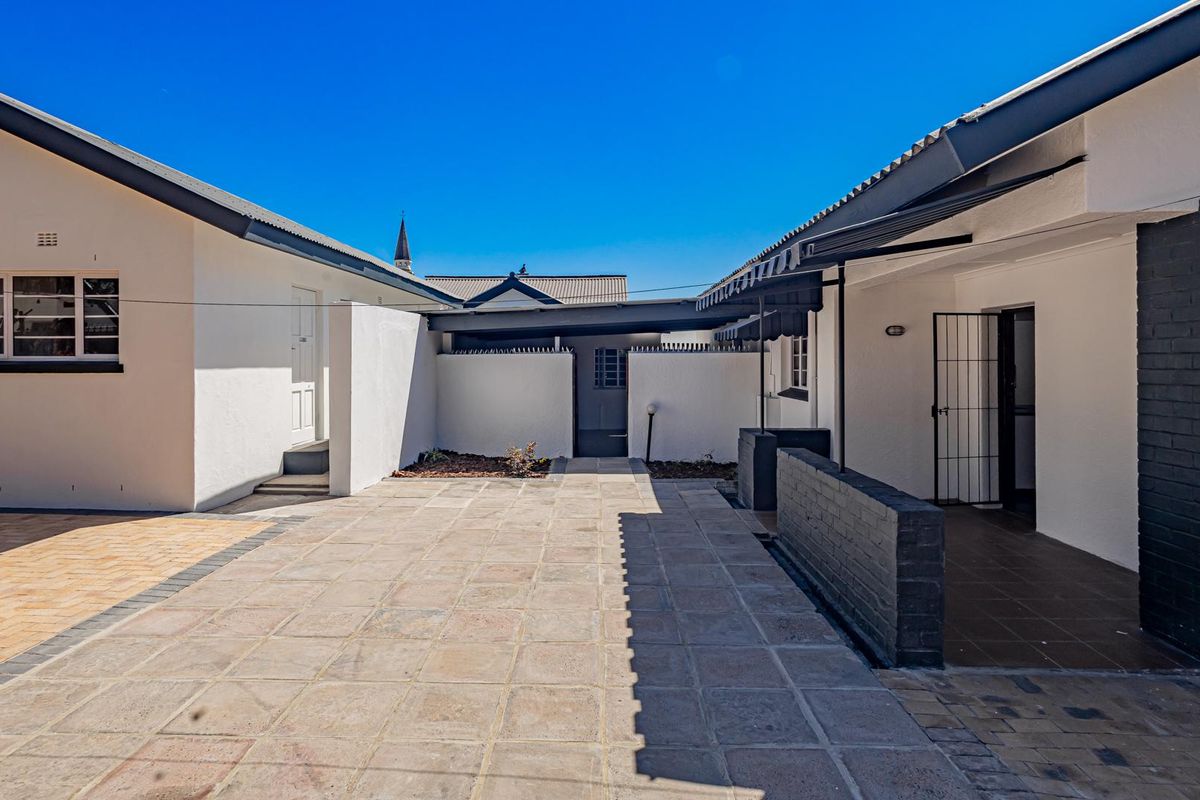 A well-maintained paved rear courtyard featuring a covered patio area, secure access points, and clean exterior finishes.