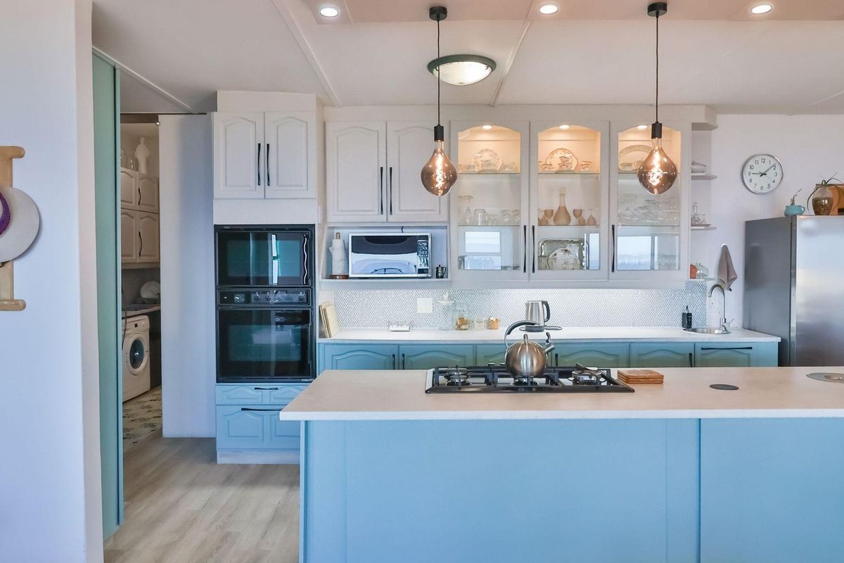 A well-appointed kitchen featuring a central island with a gas cooktop, built-in double ovens, glass-front cabinetry, and a separate scullery area.