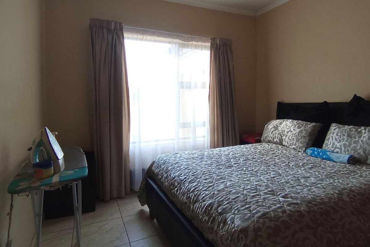 A standard bedroom featuring tiled flooring and a large window with curtains, providing natural light to the space.