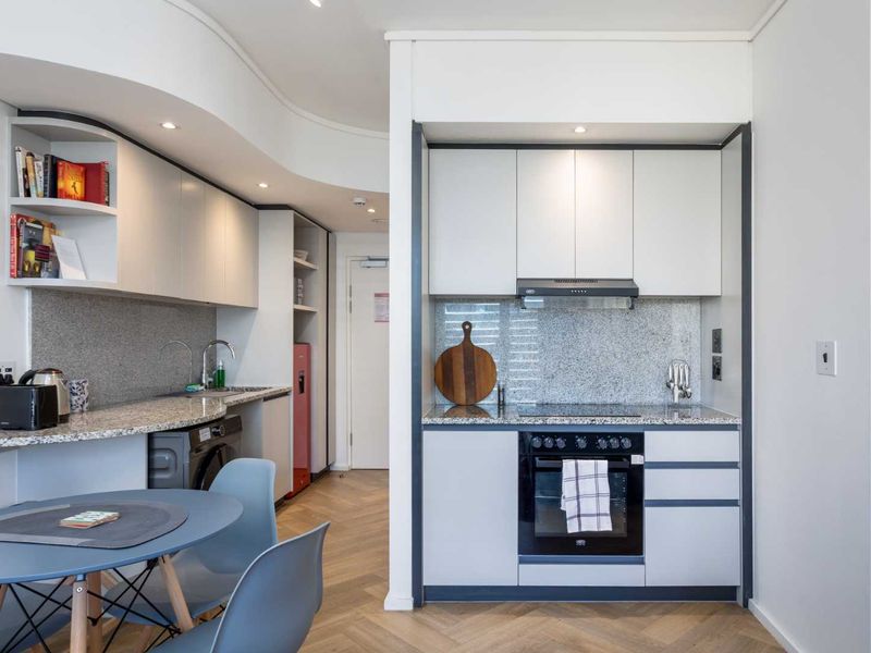 Modern compact kitchen featuring granite countertops, built-in oven, electric hob, extractor fan, and sleek cabinetry with herringbone wood flooring.