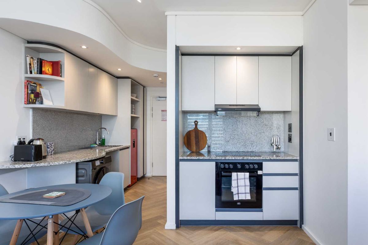Modern compact kitchen featuring granite countertops, built-in oven, electric hob, extractor fan, and sleek cabinetry with herringbone wood flooring.