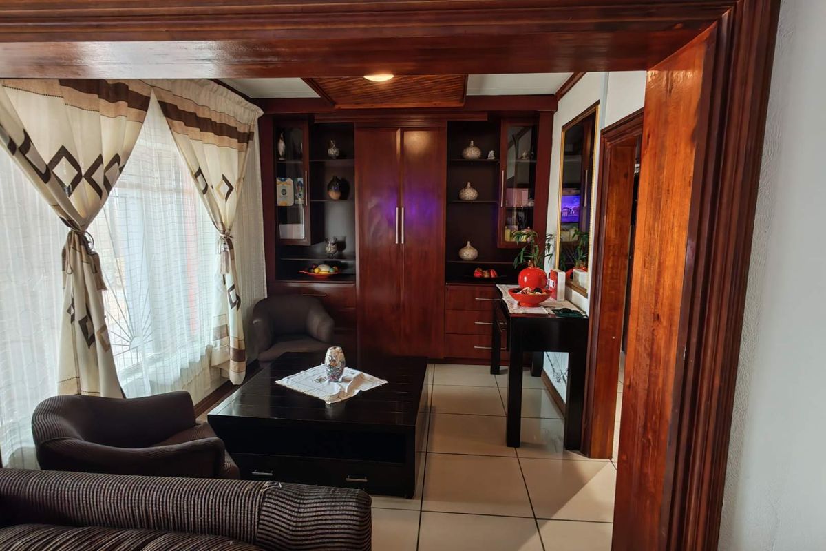 A cozy living room featuring dark wood built-in cabinetry, tiled flooring, and a warm timber-framed entryway.