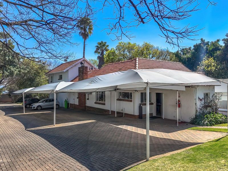 Exterior view of the office property featuring a paved driveway, a large covered carport area, and well-maintained surrounding lawn and garden.