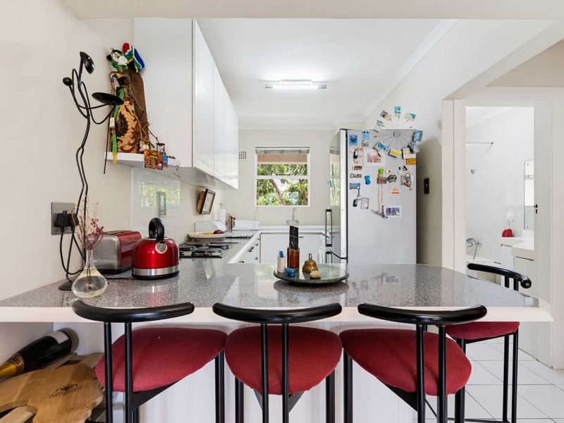 A functional kitchen featuring white cabinetry, a breakfast bar with laminate countertops, and tiled flooring, with an adjacent view into the bathroom area.