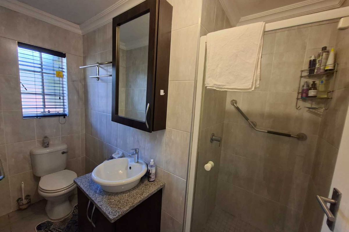 A functional bathroom featuring a vanity with a vessel sink, a toilet, and a glass-enclosed shower with a safety grab rail.