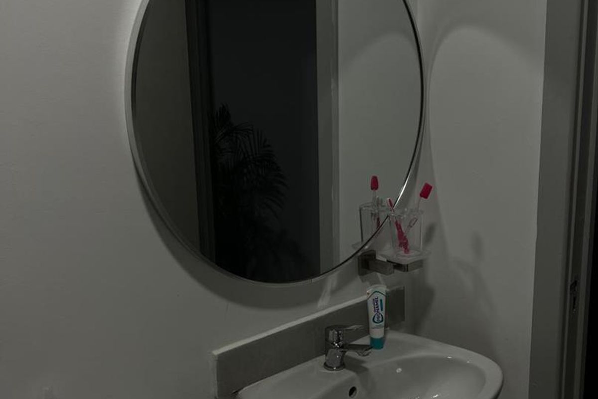 A functional bathroom featuring a white vanity cabinet with a ceramic basin, chrome faucet, and a circular wall-mounted mirror.