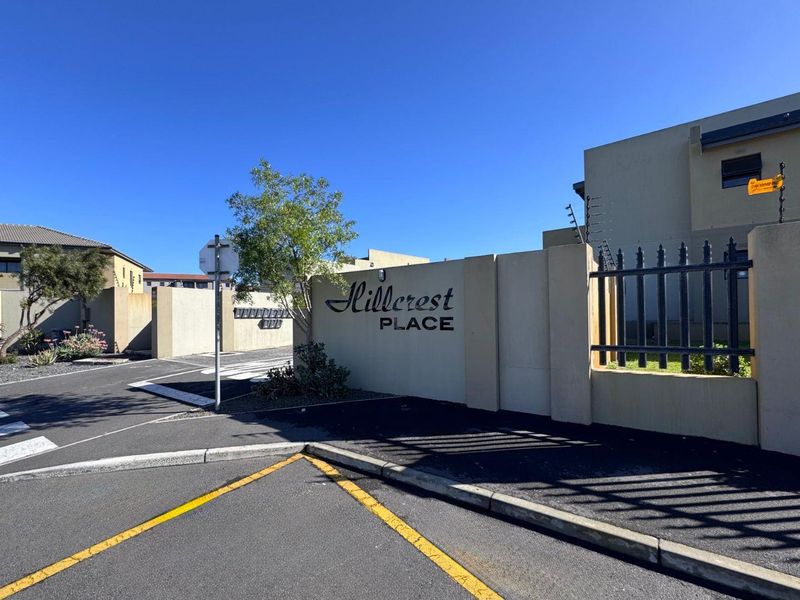 Entrance view of Hillcrest Place apartment complex featuring a perimeter wall, security fencing, and clear signage.