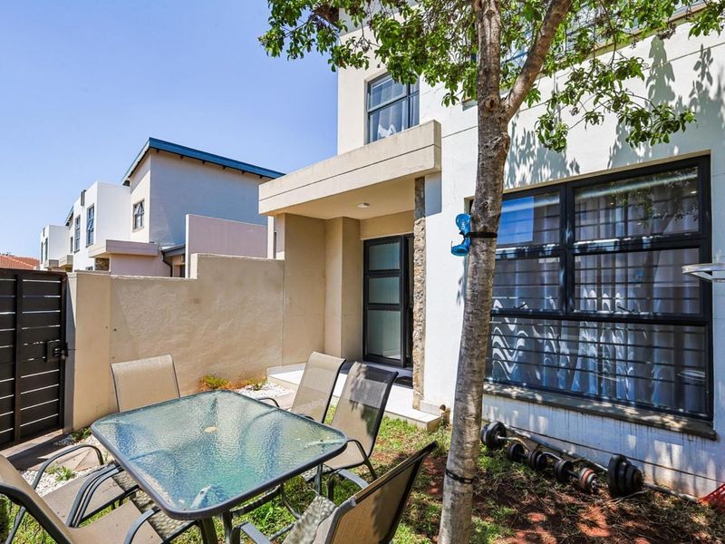 A private rear courtyard featuring a paved area, boundary wall with metal gate, and modern aluminium window frames with security bars.