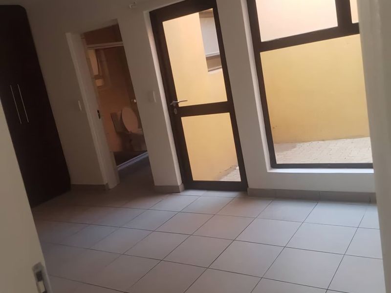 A clean, empty bedroom featuring tiled flooring, a built-in wardrobe, and direct access to a private outdoor courtyard area.