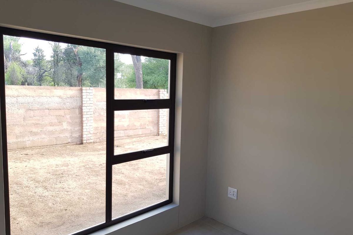 A bright, empty bedroom featuring neutral walls, tiled flooring, and a large window with dark frames overlooking the rear yard.