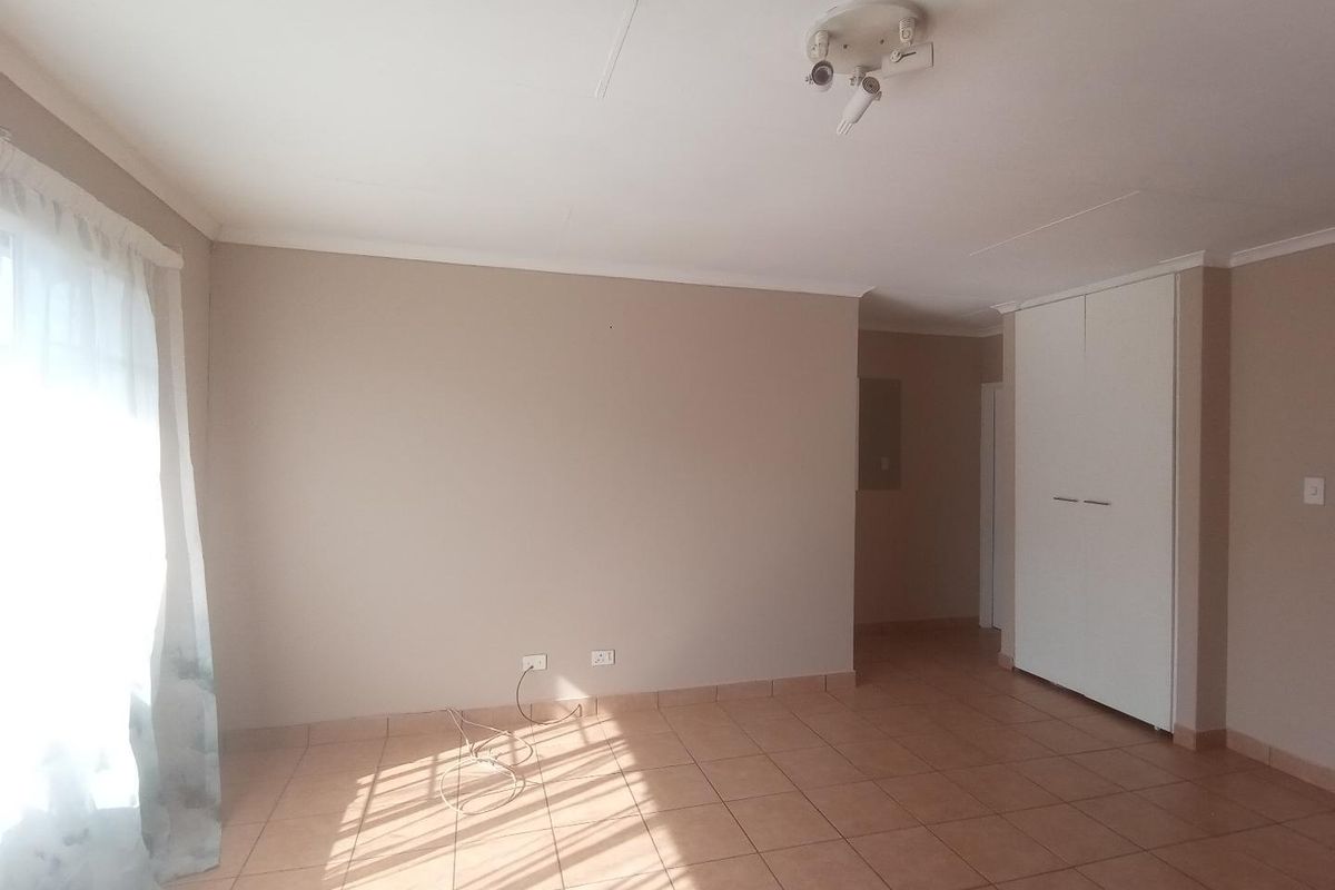 A bright, empty bedroom featuring neutral wall tones, tiled flooring, and built-in storage cupboards.