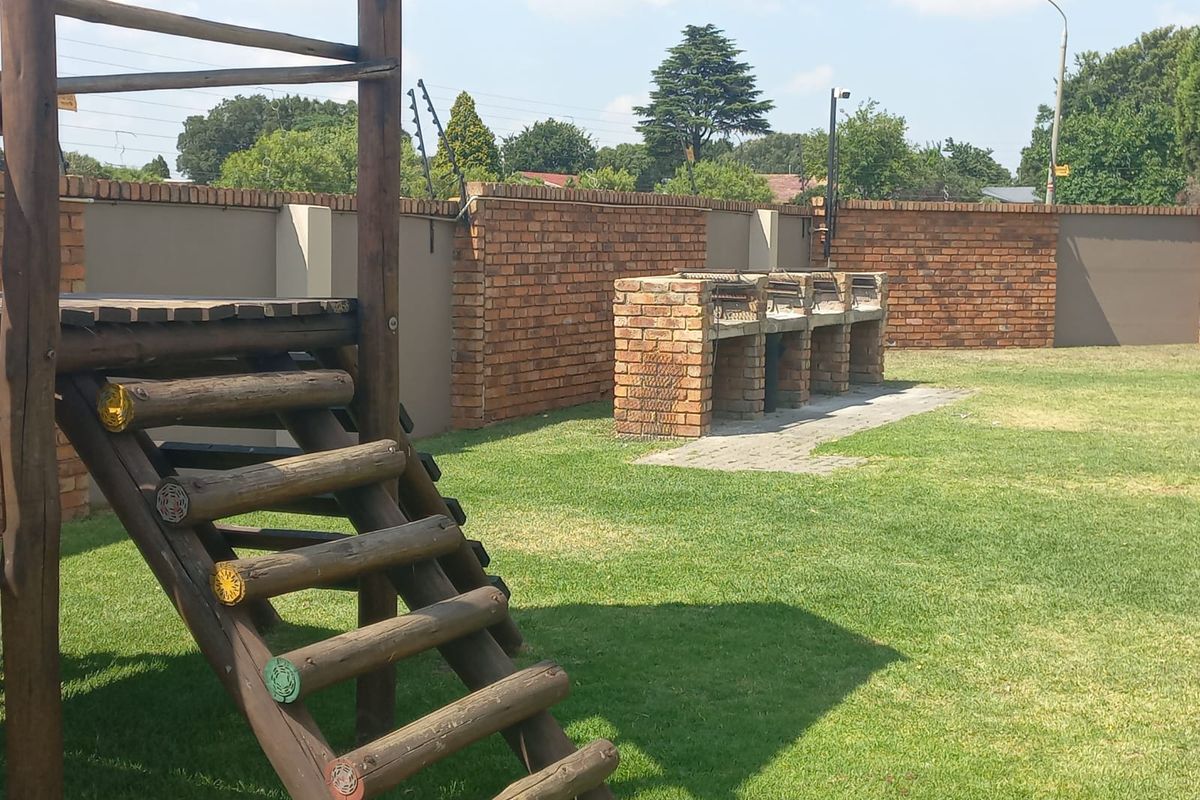 A spacious rear garden featuring a built-in brick braai area, secure perimeter wall with electric fencing, and a well-maintained lawn.