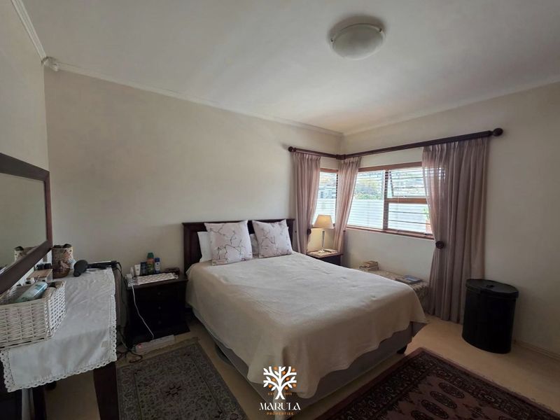 A standard bedroom featuring neutral wall finishes, corner window placement with fitted blinds, and a simple ceiling light fixture.