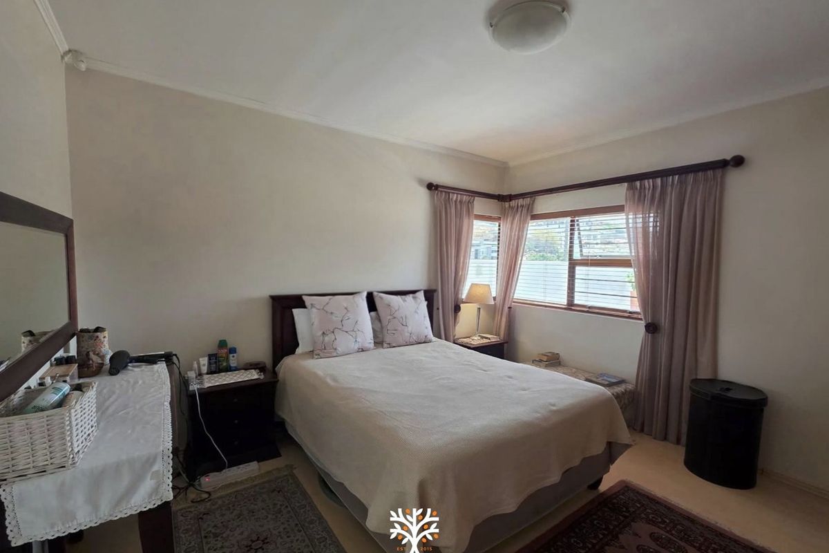 A standard bedroom featuring neutral wall finishes, corner window placement with fitted blinds, and a simple ceiling light fixture.