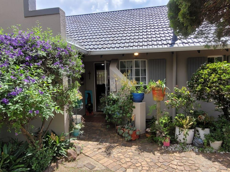 Front entrance of the townhouse featuring a paved walkway, established garden beds, and a tiled roof facade.
