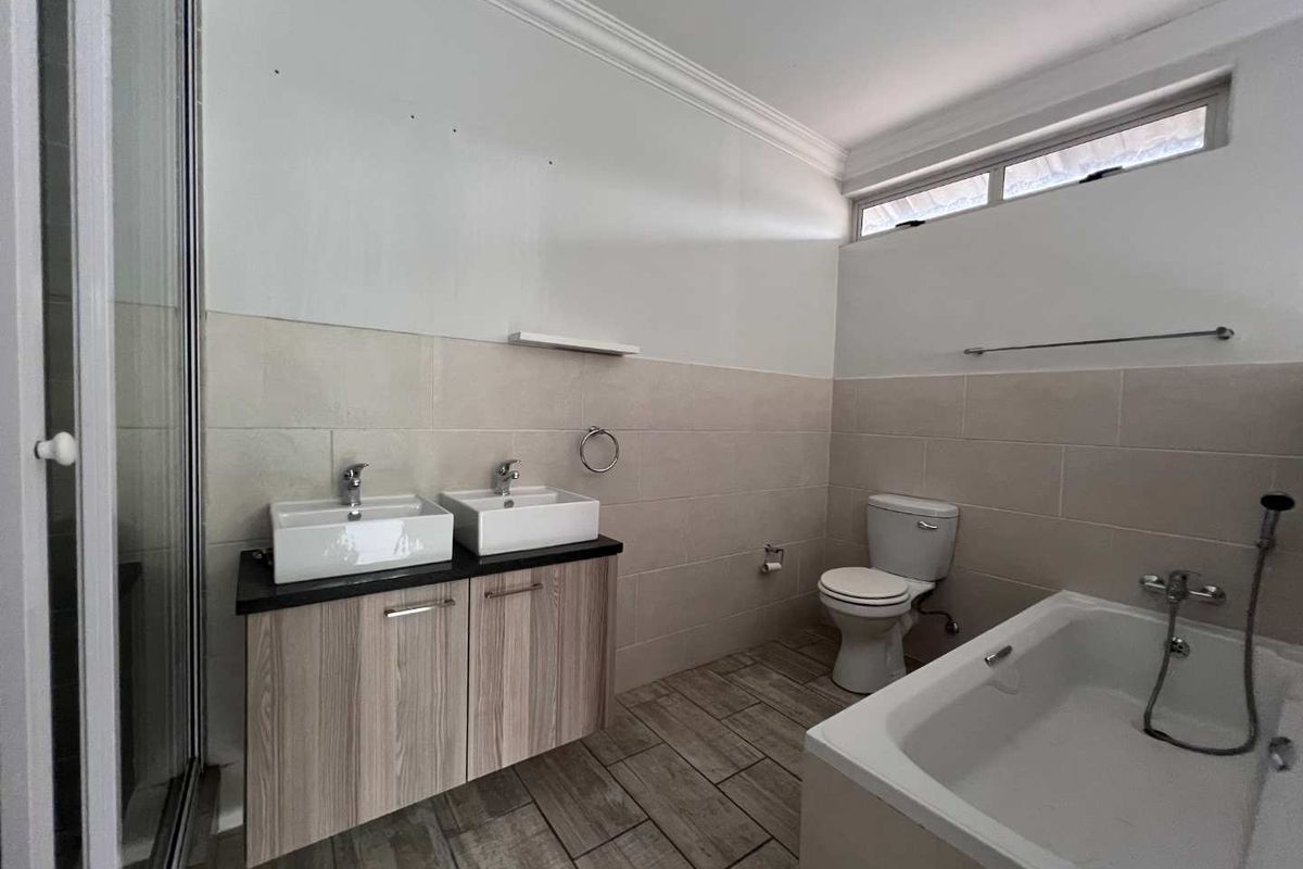 Modern bathroom featuring a double vanity with vessel sinks, a separate bathtub, a glass-enclosed shower, and neutral wall and floor tiling.