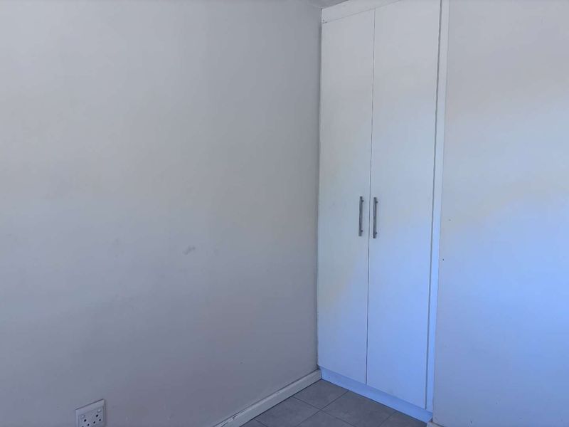 A simple, empty bedroom corner featuring a white built-in cupboard and tiled flooring.