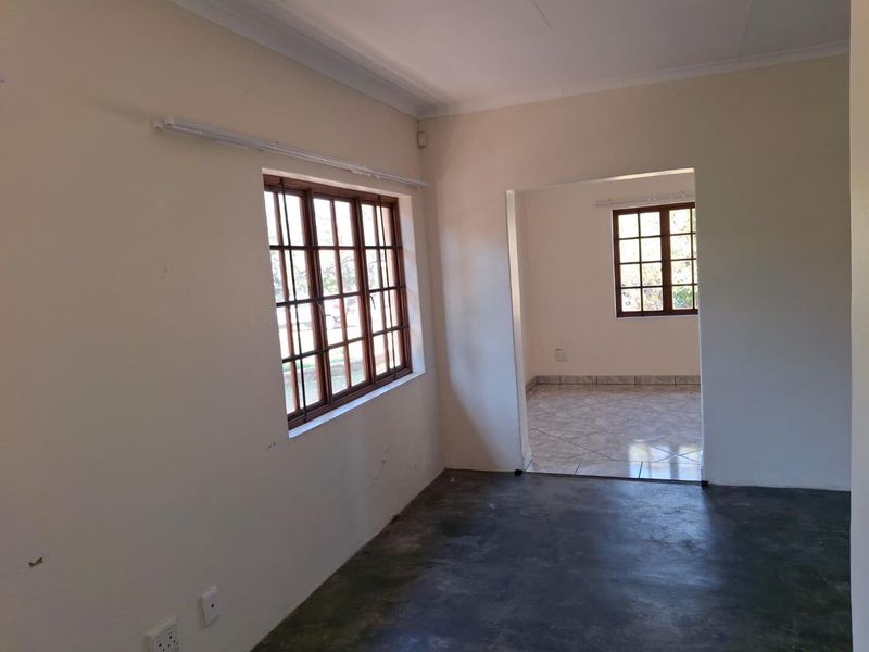 An empty living area featuring wooden window frames, tiled and concrete flooring, and neutral walls, offering a blank canvas for renovation.