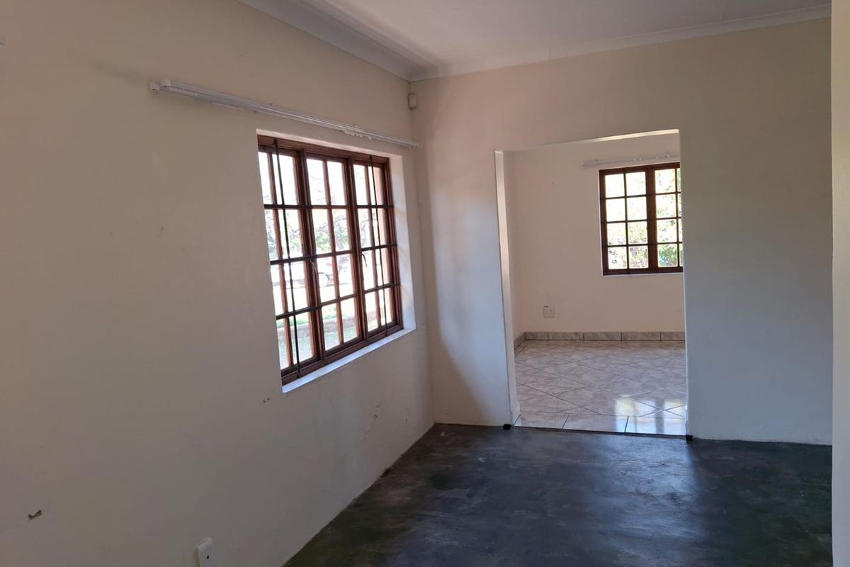 An empty living area featuring wooden window frames, tiled and concrete flooring, and neutral walls, offering a blank canvas for renovation.