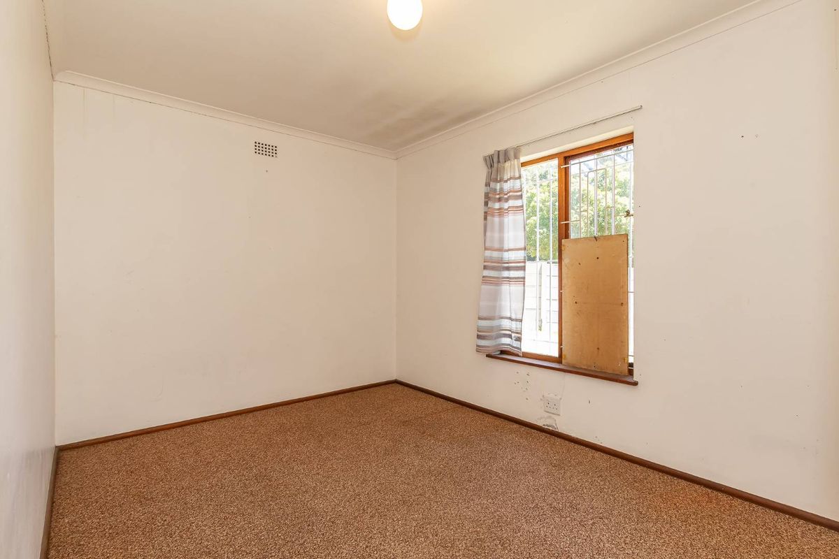A vacant bedroom featuring carpeted flooring, a window with security bars, and a ceiling light fixture.